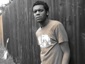 The guitarist Gary Clark Jr. rests on a wooden fence.